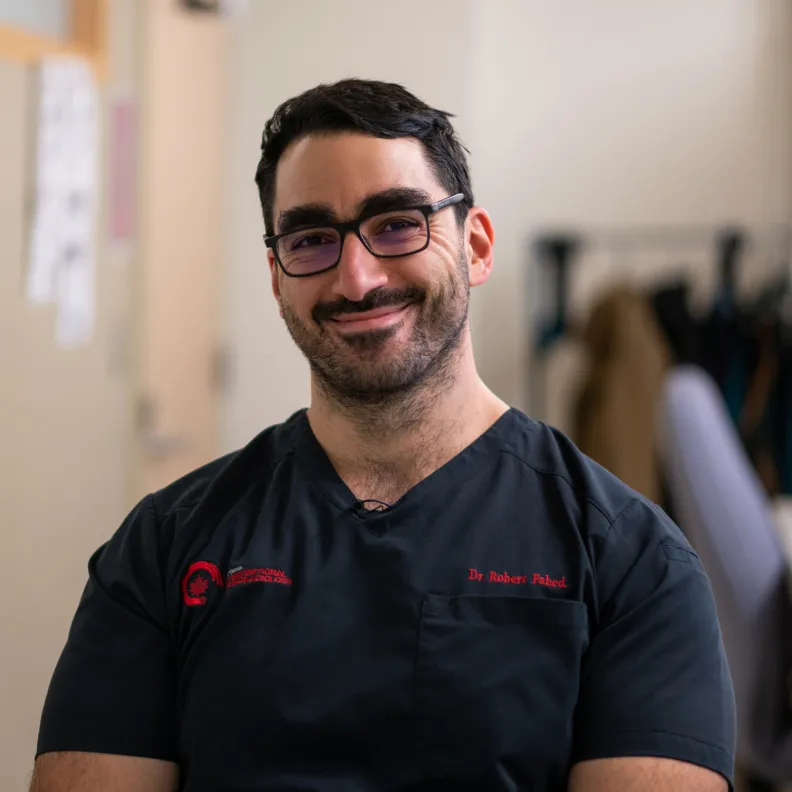 A man wearing dark blue scrubs smiles at the camera