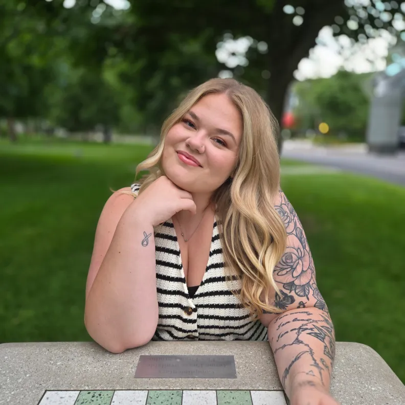 A woman sits at an outdoor chess table and smiles at the camera