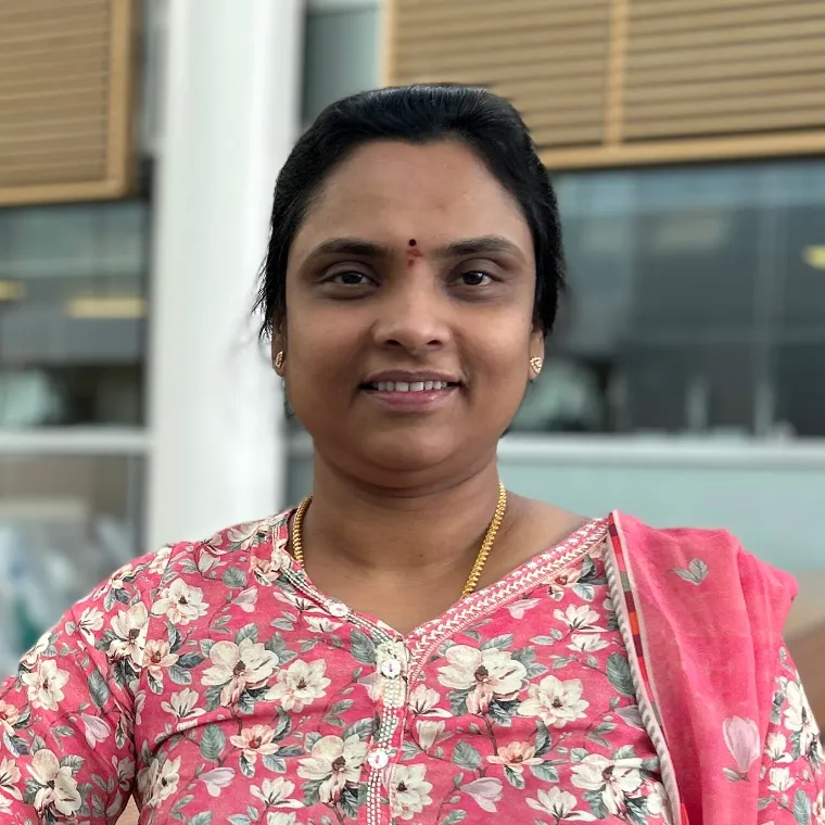 A woman wearing a pink, floral sari smiles at the camera