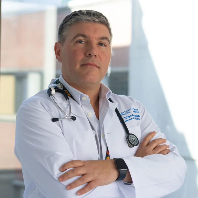 Man in lab coat and stethoscope looks at camera