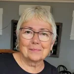 An older woman with glasses and short grey hair smiles at the camera